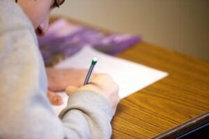 Person writing on paper with a pencil