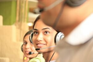 Two customer service workers wearing headsets at computers in a bright office
