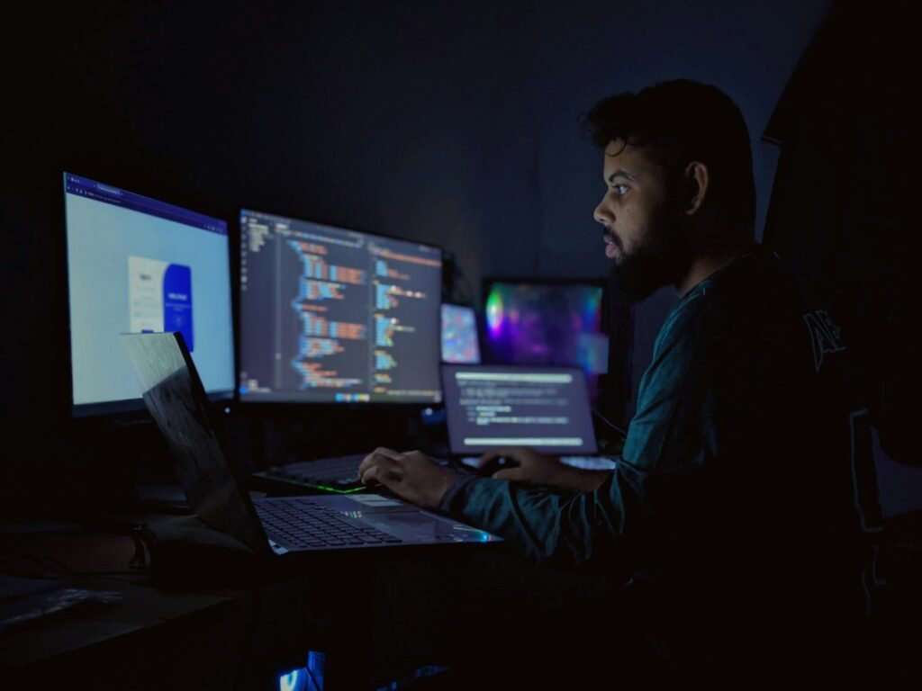 Developer sitting in front of three monitors, comparing Cursor vs Claude Code for AI-assisted coding